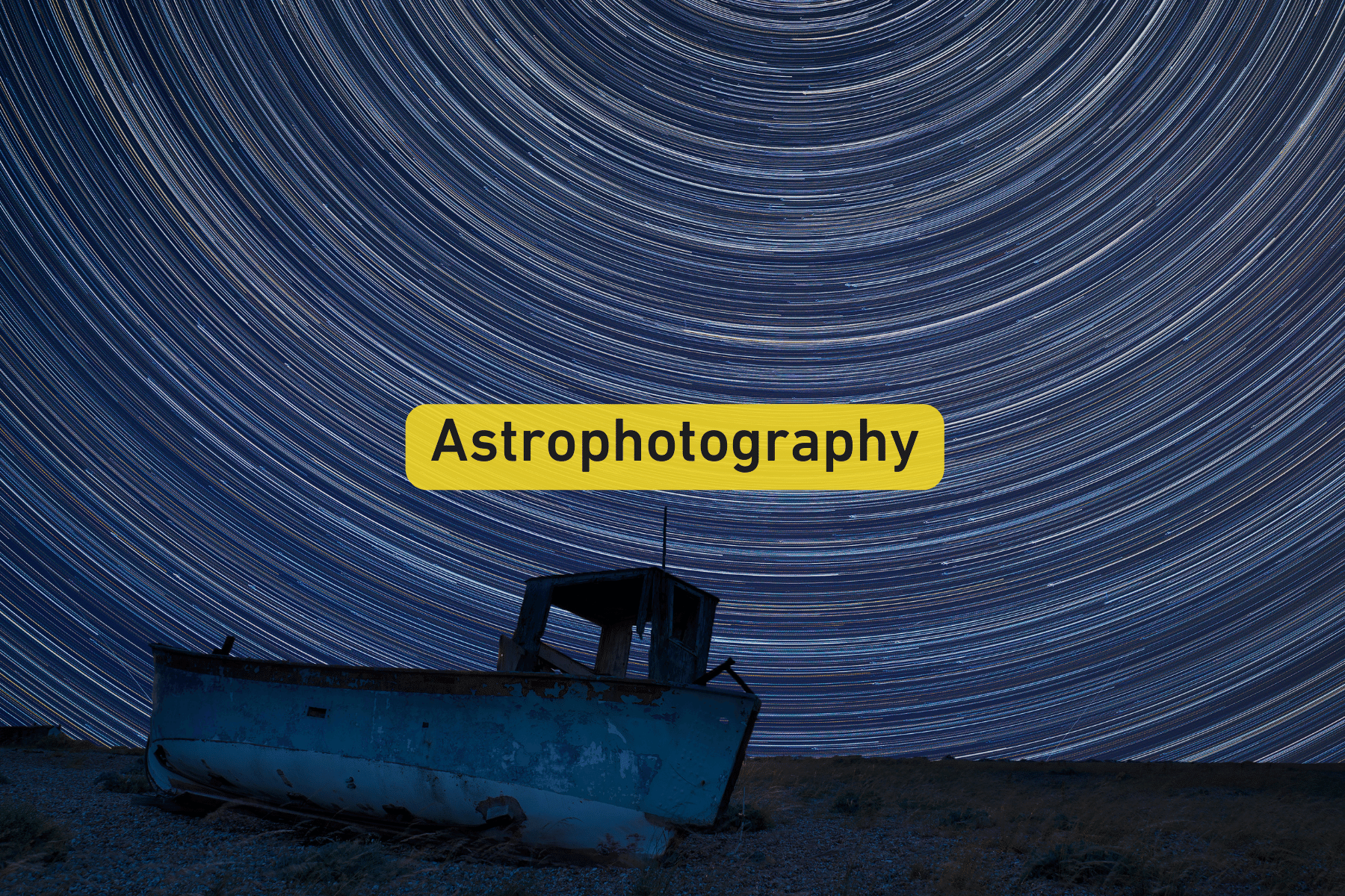 Night sky with star trails above a weathered boat on the ground.