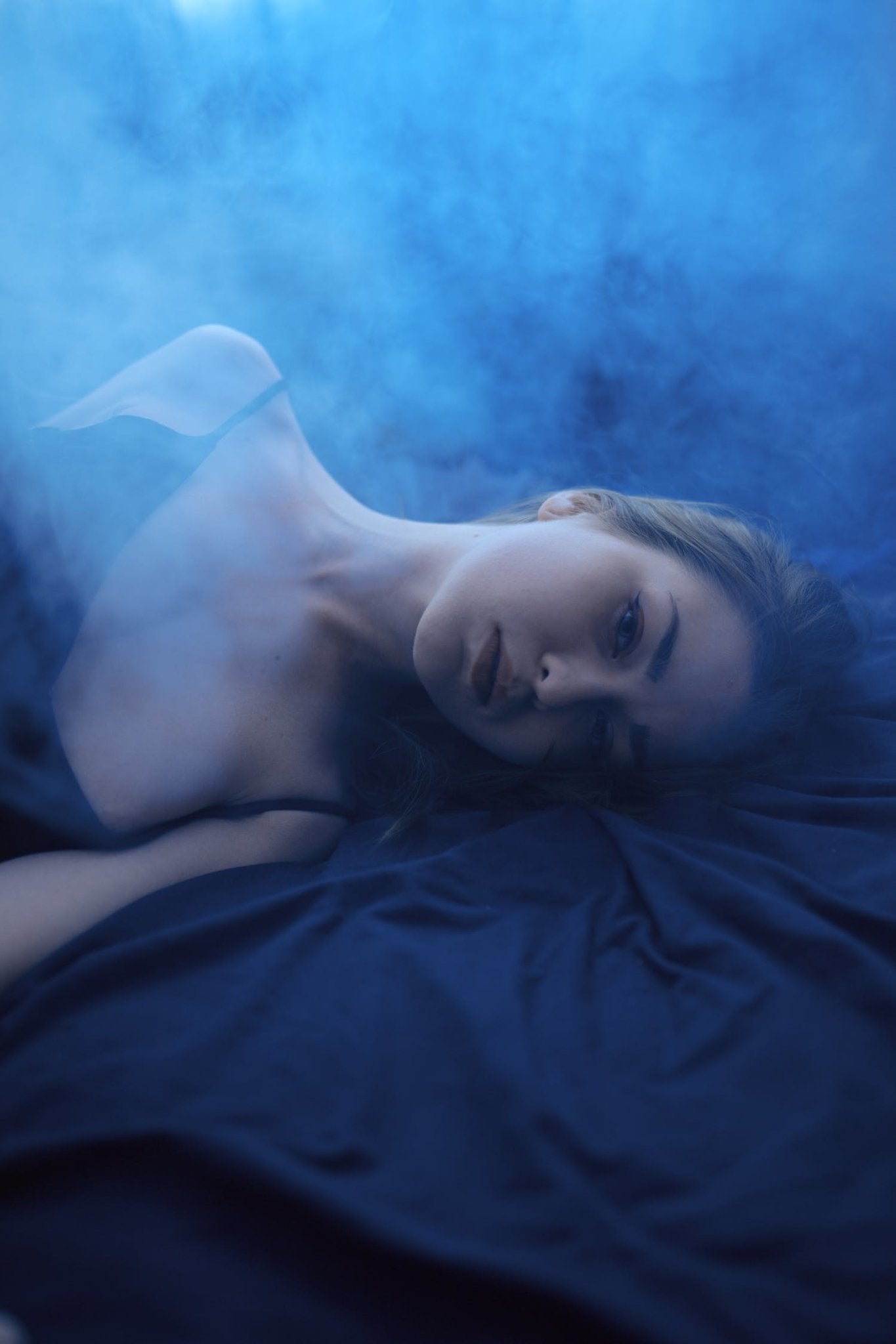 Blue atmospheric fog surrounding a woman lying on a dark bed