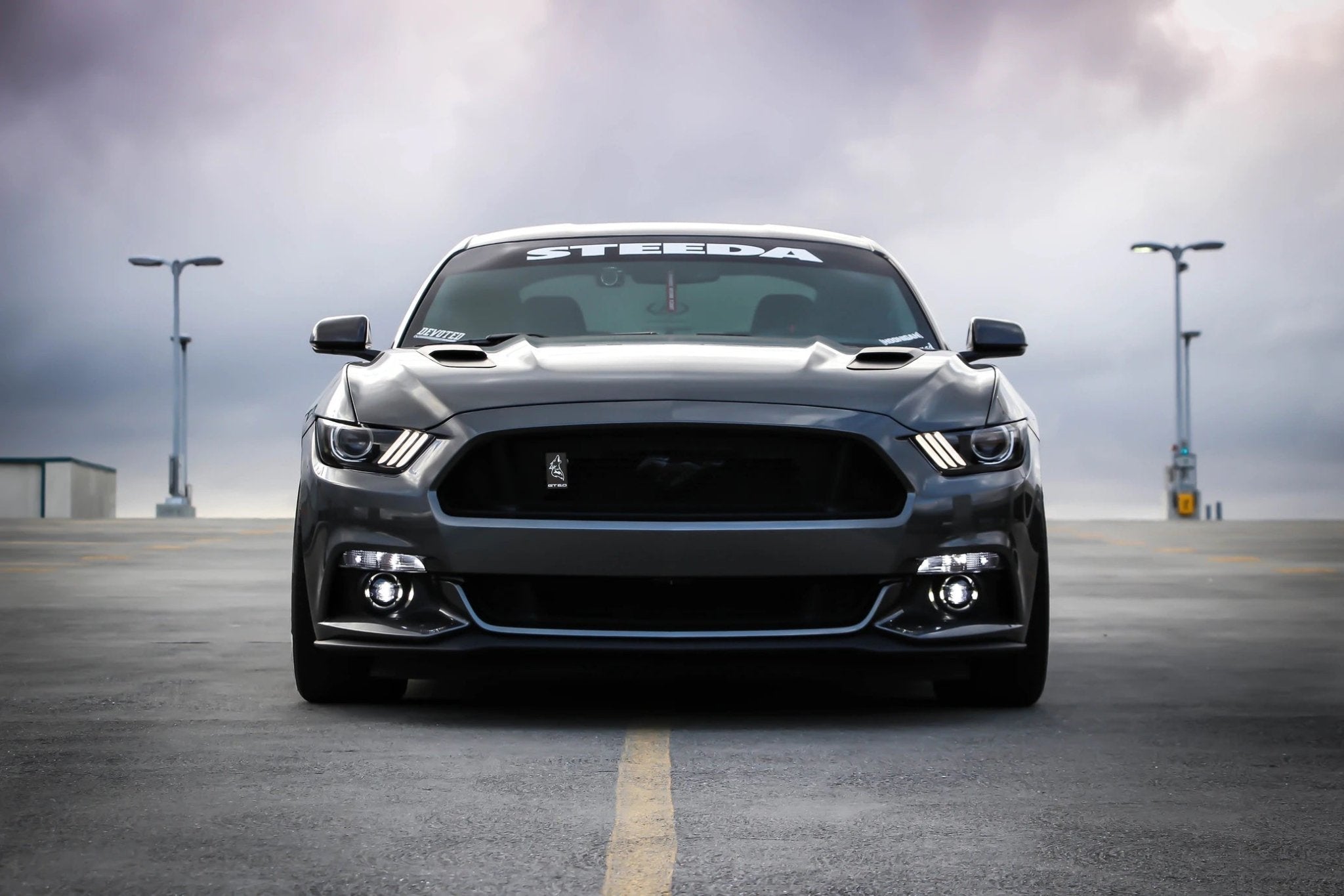 Black Ford Mustang with Steeda branding parked in an empty lot under cloudy sky.