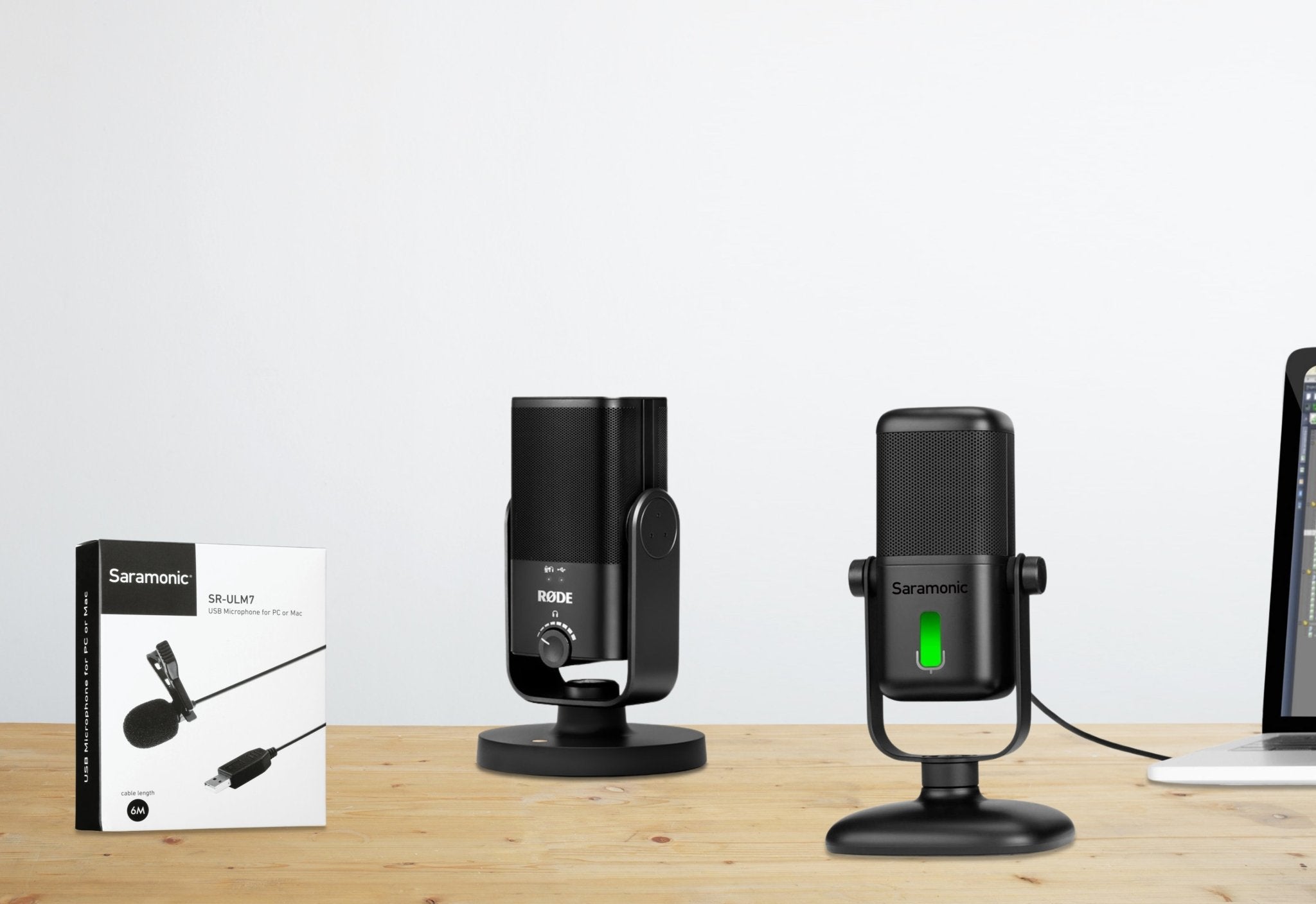 Black microphones on a wooden desk beside a product box and laptop.