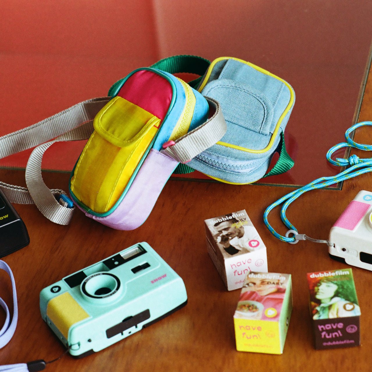 Colorful camera bags and analog cameras on a wooden surface with film boxes.