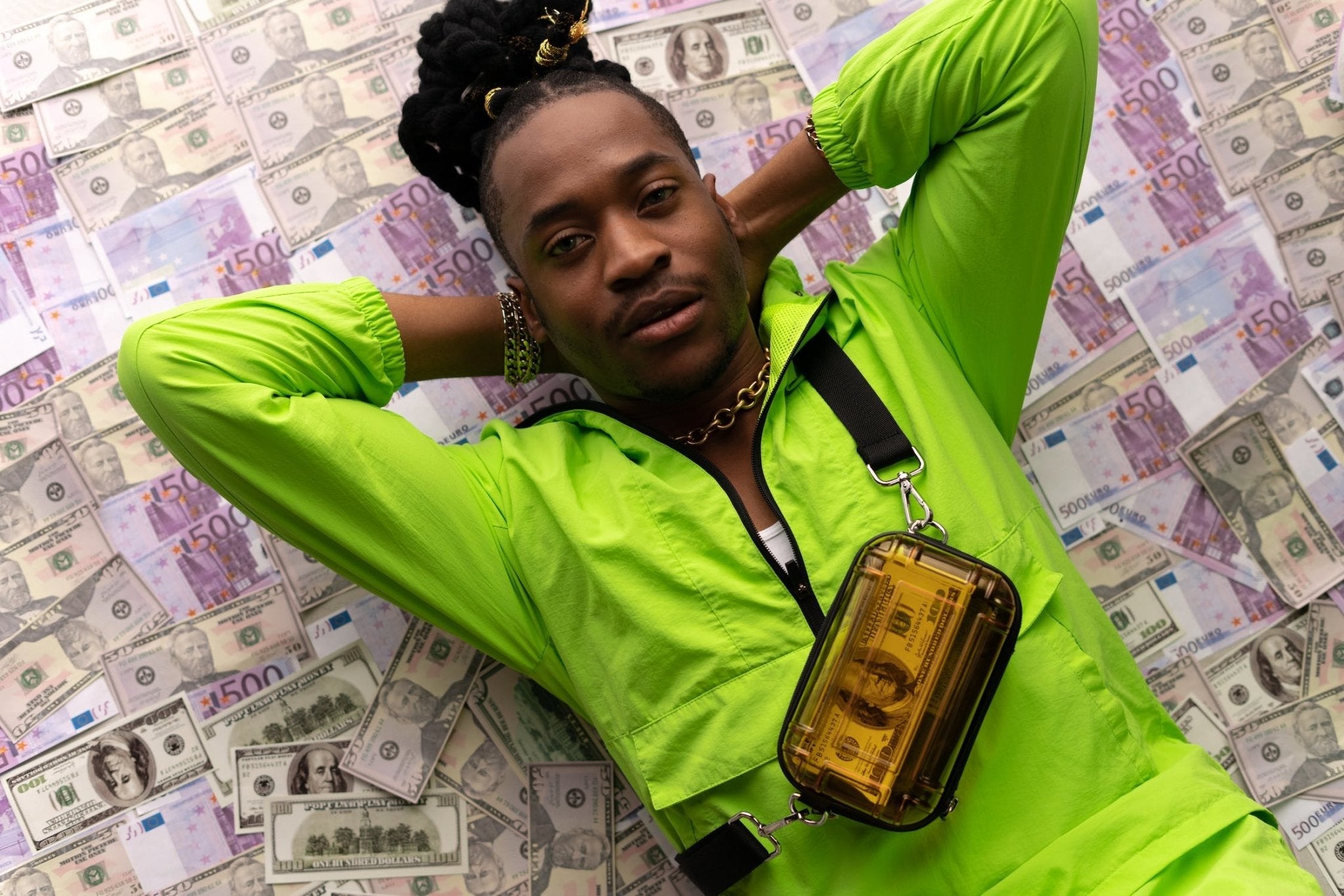Man in neon green jacket laying on a bed of money with a golden clear bag.