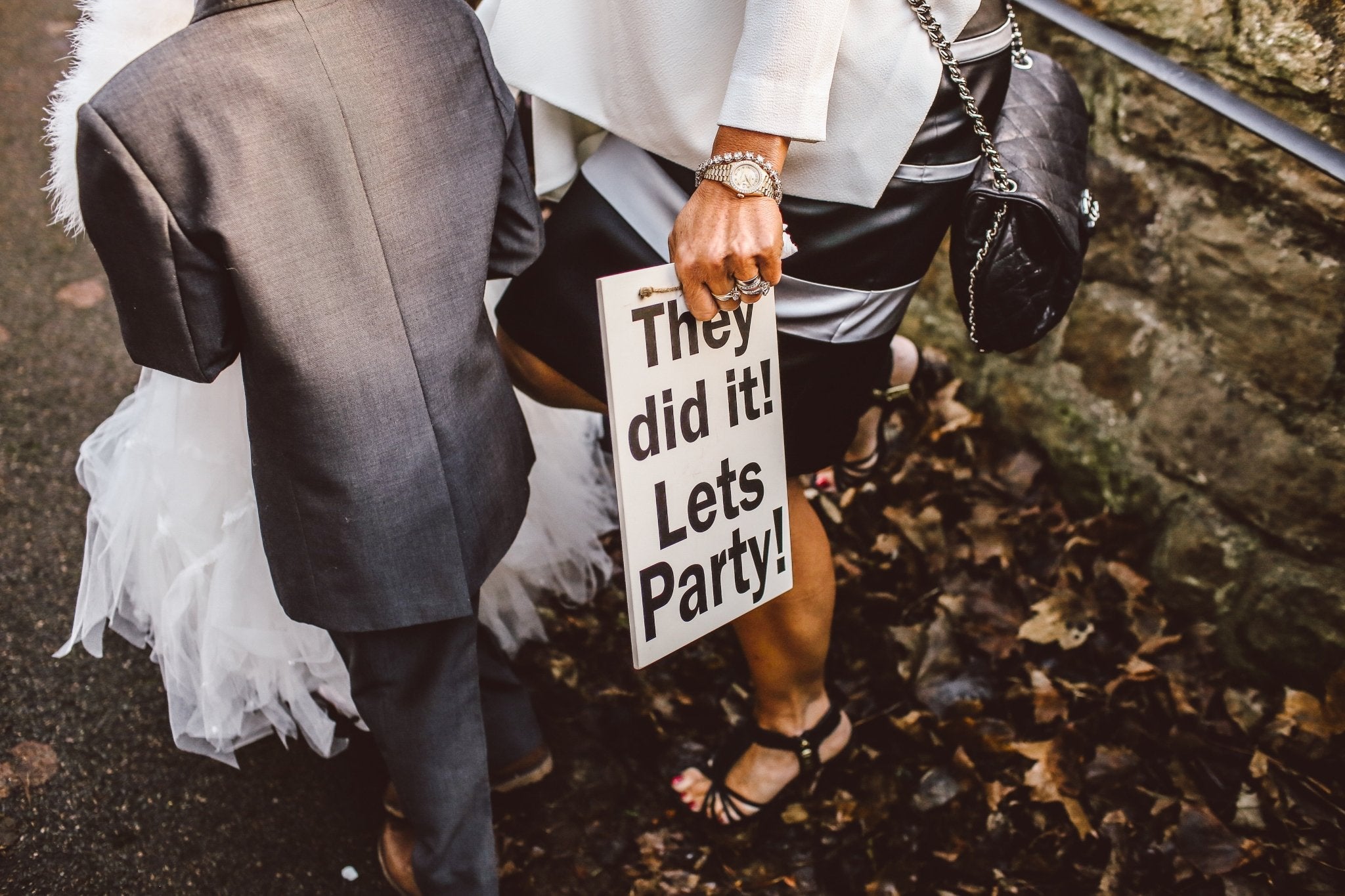Woman in a white outfit holding a sign reading 'They did it! Let's Party!' with a child in a suit.