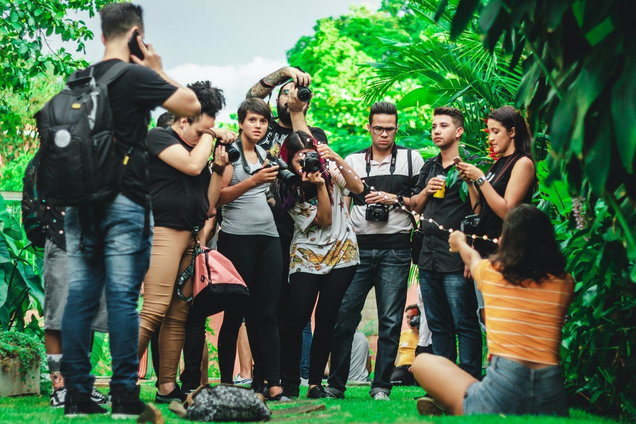 Group of photographers with cameras capturing a subject outdoors surrounded by greenery.