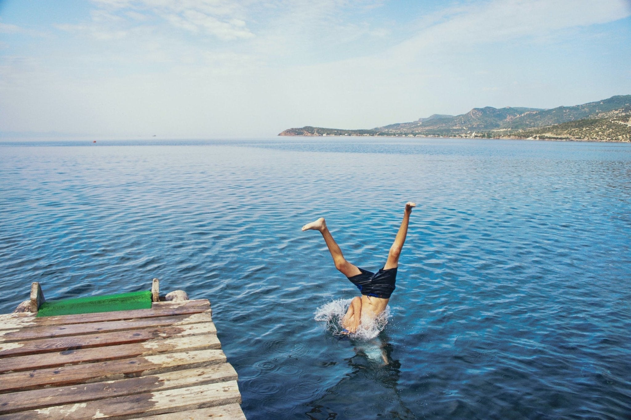 Boy diving into the clear blue water from a wooden dock