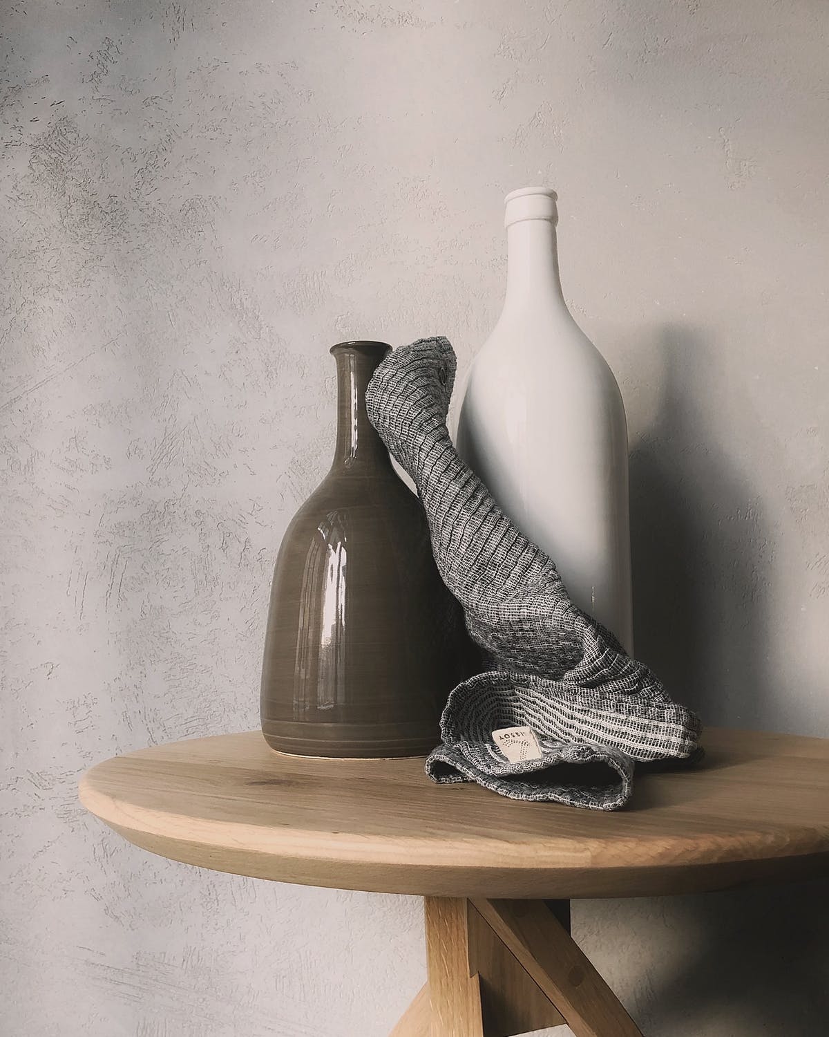 Two ceramic vases, one dark brown and one white, draped with a soft gray cloth on a wooden table.