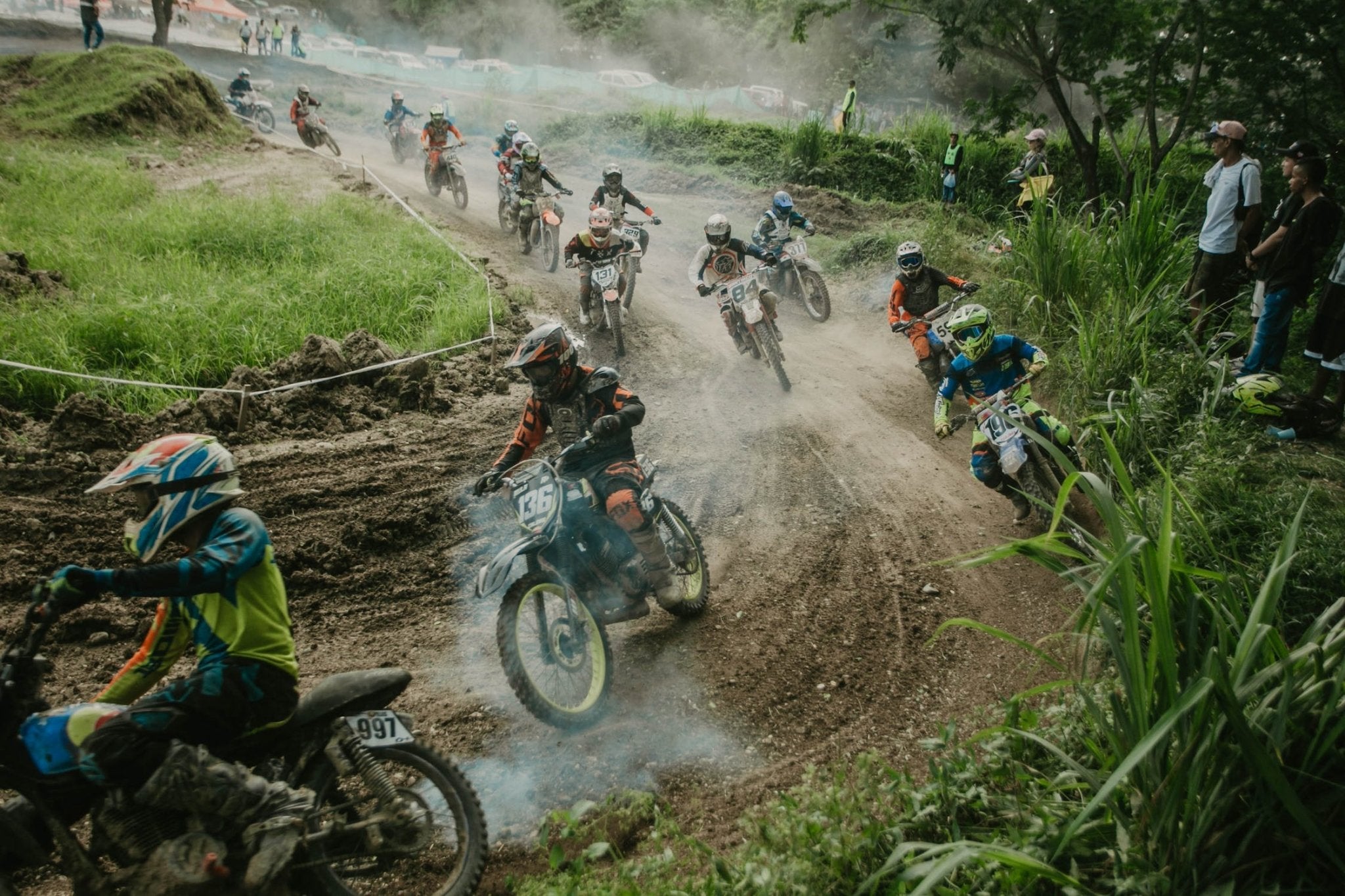 colorful motocross riders racing on a dirt track with dust and grass surrounding the scene