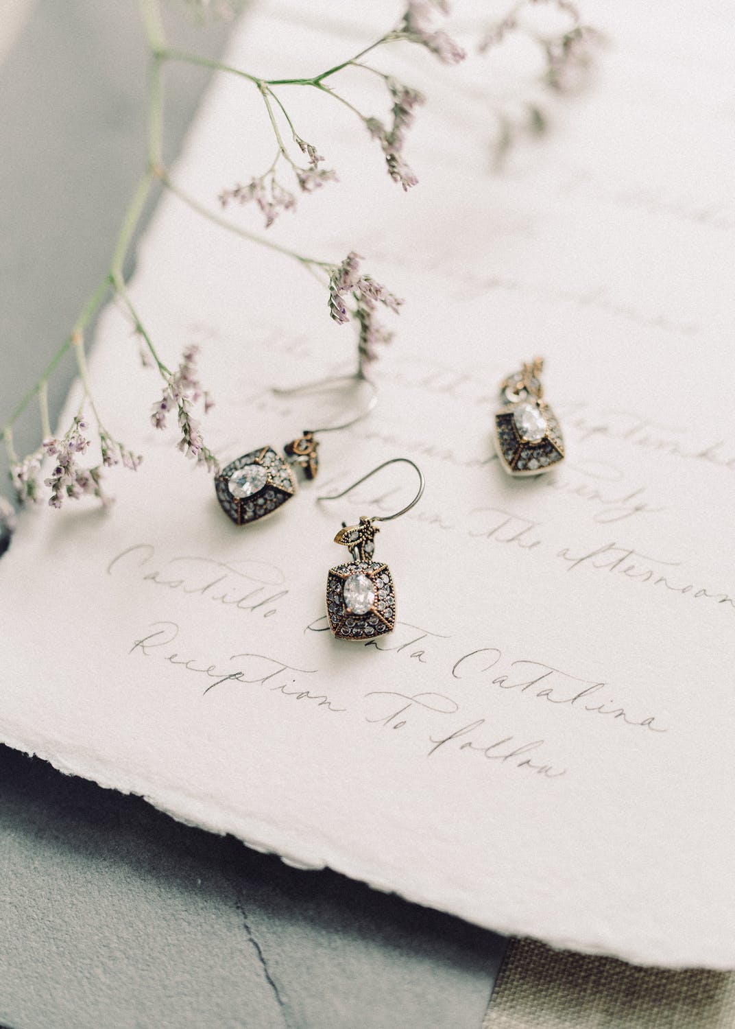 Gold and silver earrings on textured paper with delicate floral accents.