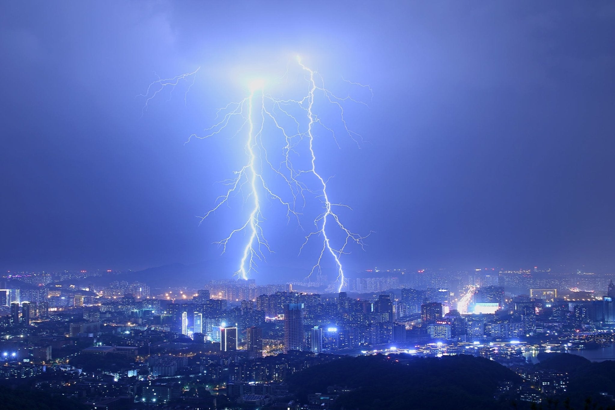 Bright blue lightning strikes over a city skyline during a stormy night.