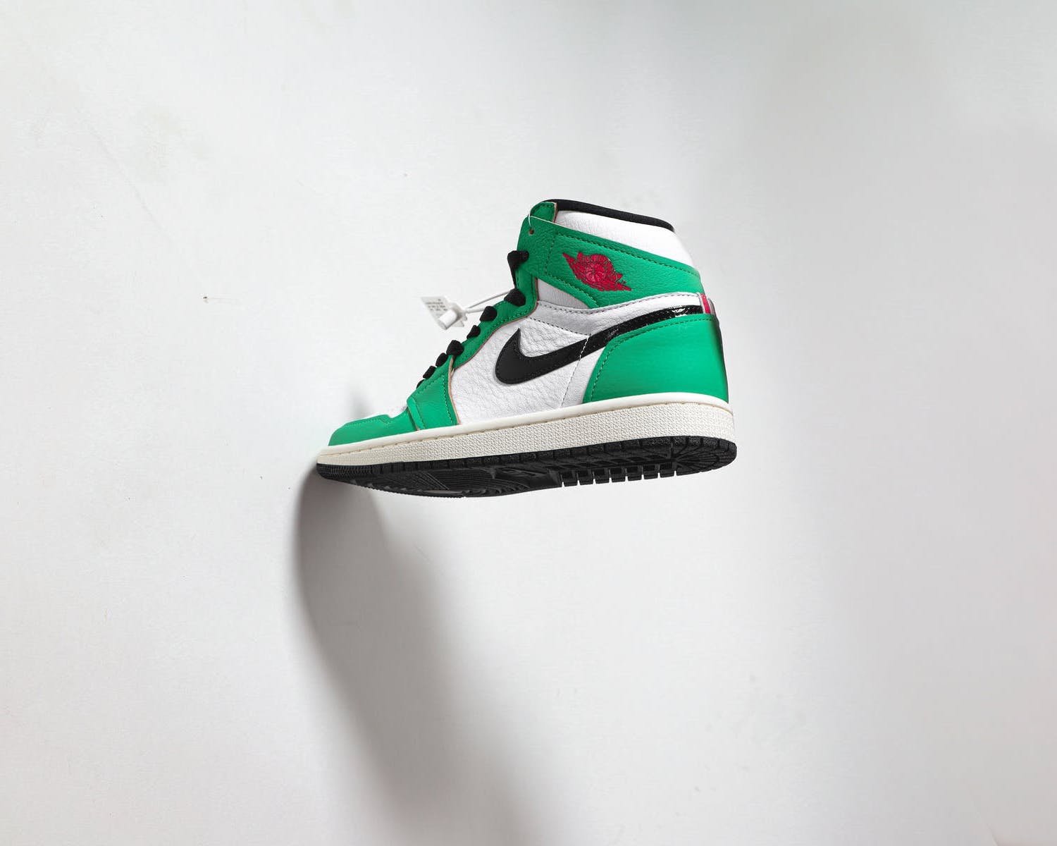 Green and white Nike high-top sneaker with black details, hanging against a white background.