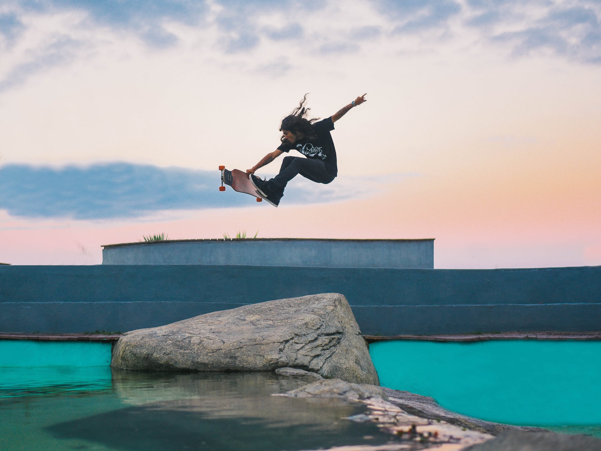 Skateboarder performing a trick over a rock formation at sunset.