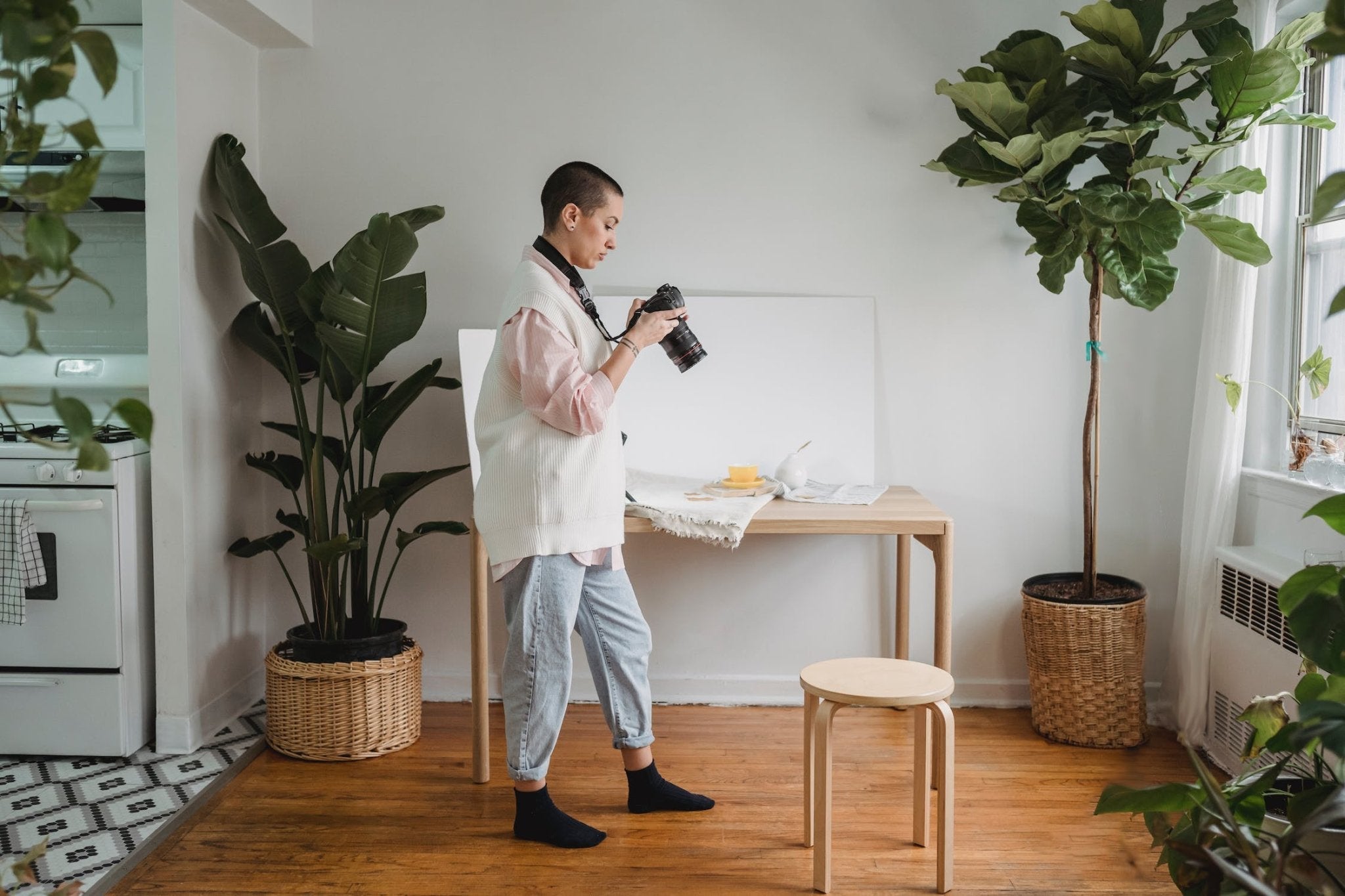 Young woman with a camera in a bright, plant-filled room, focusing on a food setup.