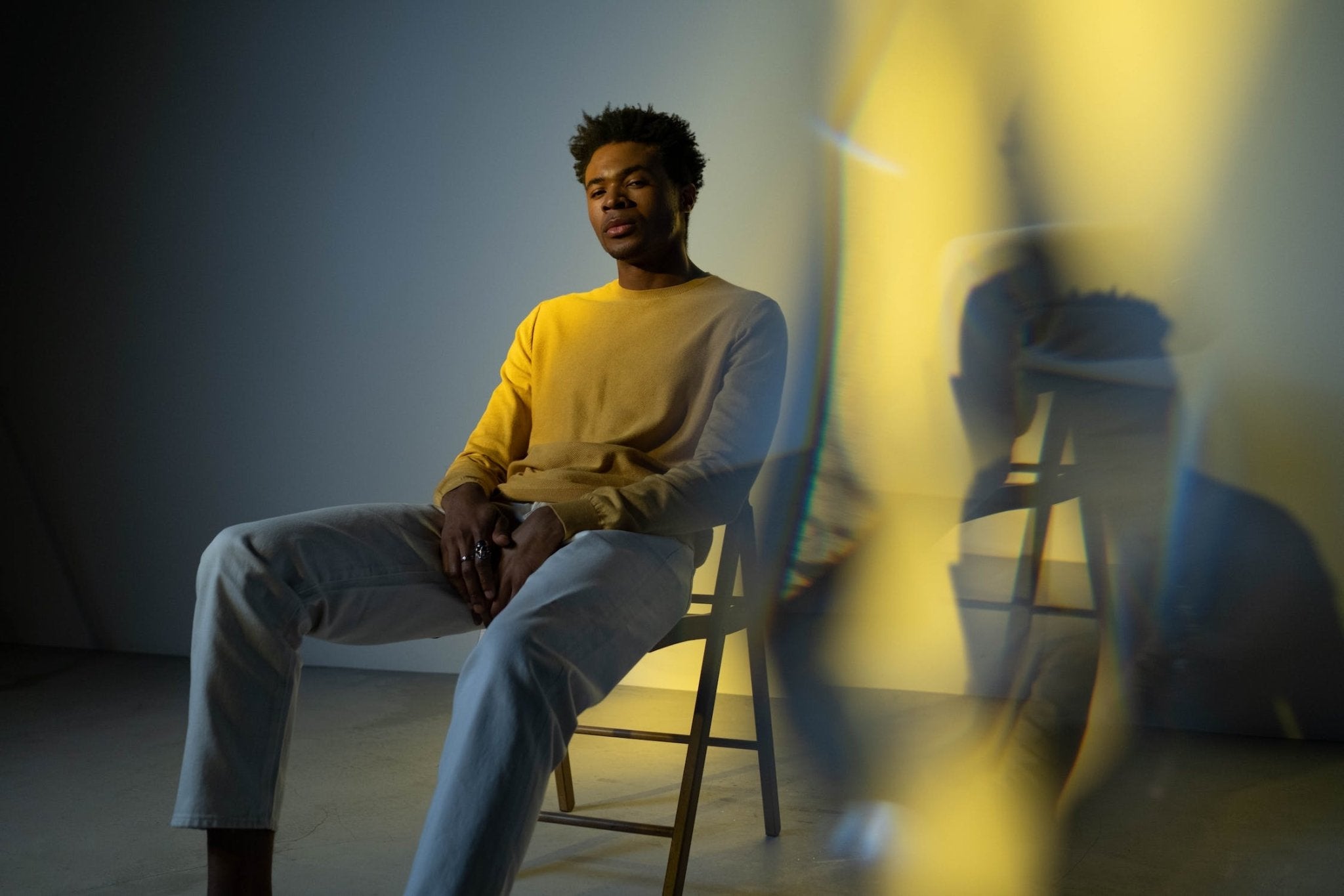 Yellow sweater, sitting man on a chair, light refraction creating abstract shapes.