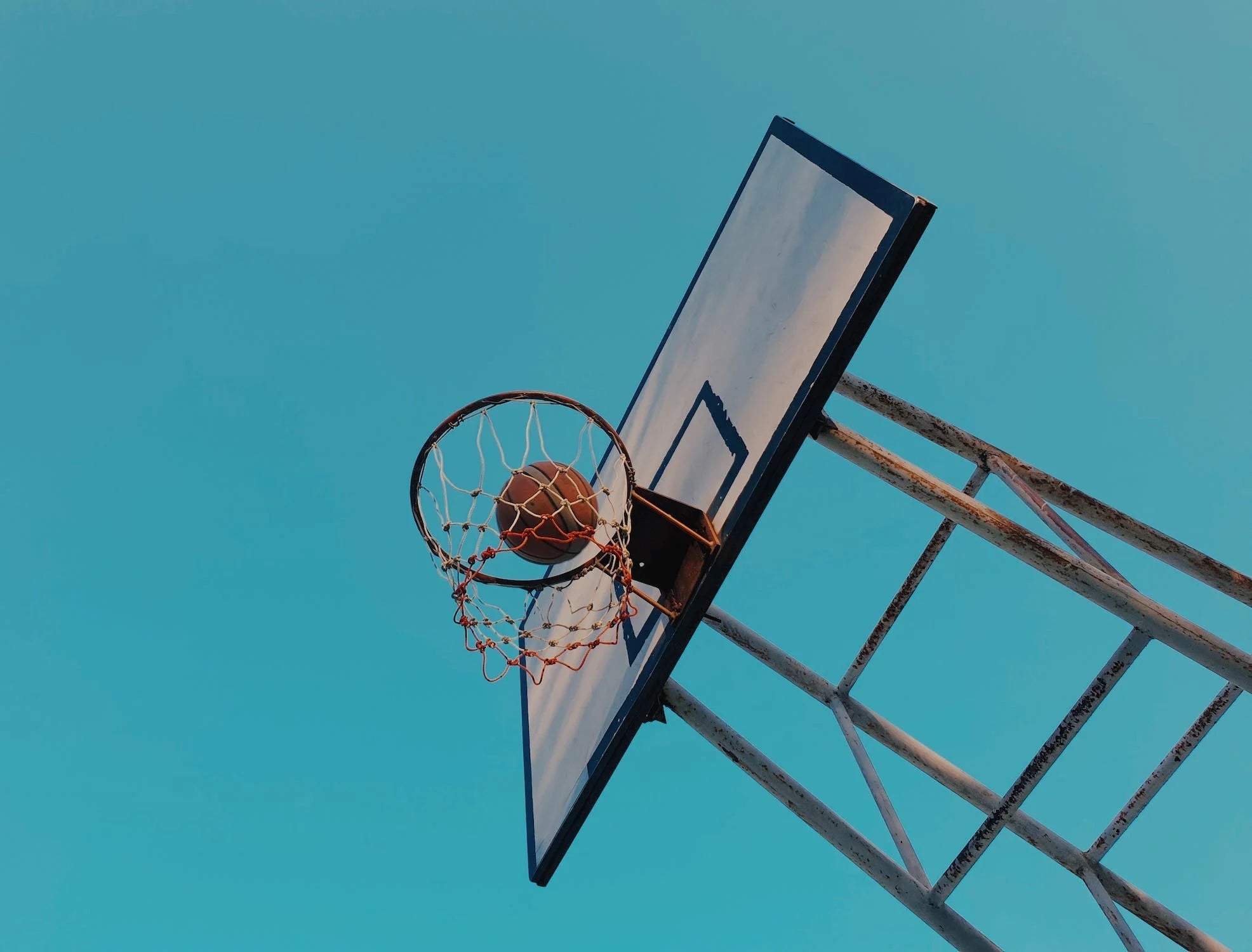 Basketball hoop with a ball in the net against a clear blue sky.