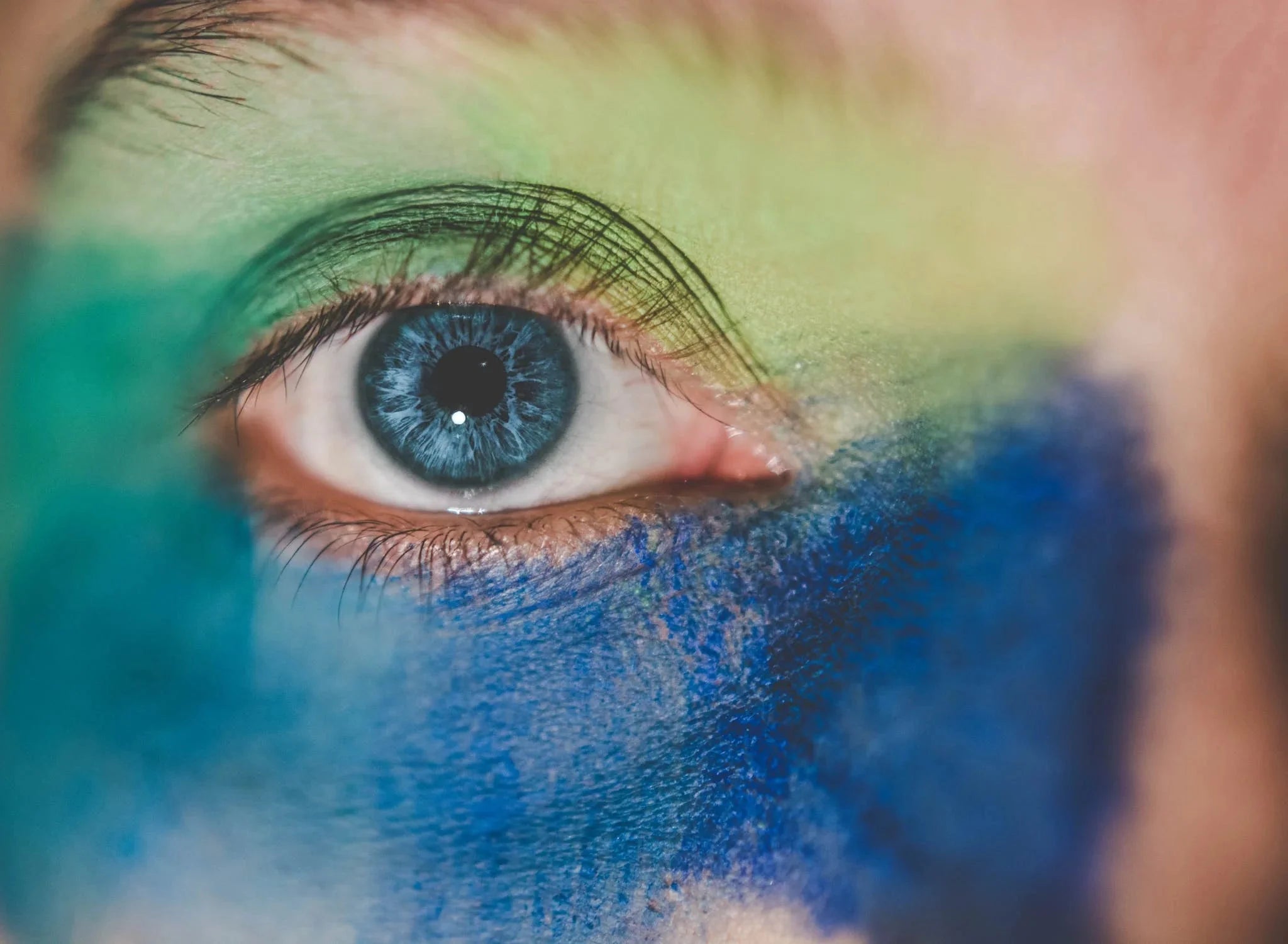Blue eye with colorful face paint in green and blue shades.