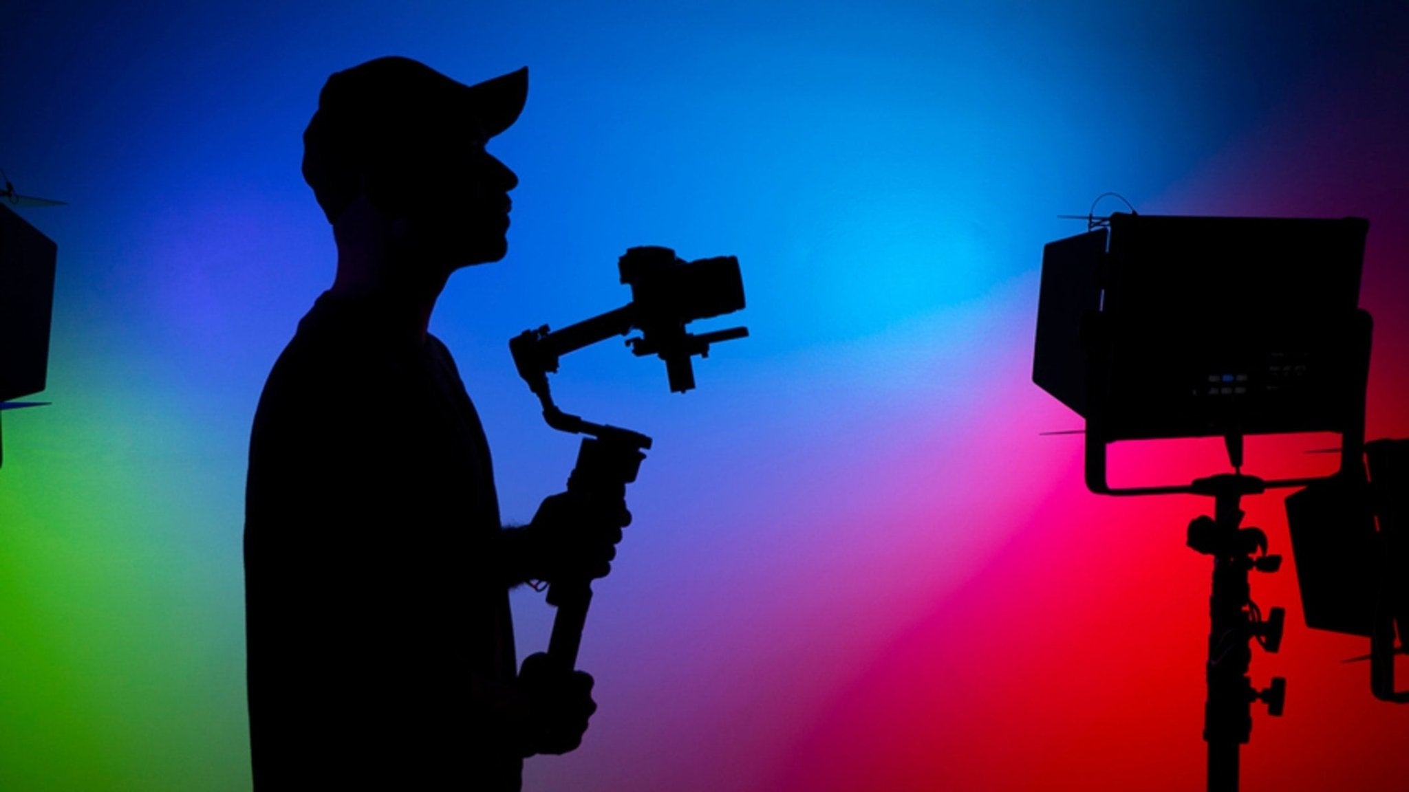 Silhouette of a person holding a camera gimbal with colorful studio lights in the background.