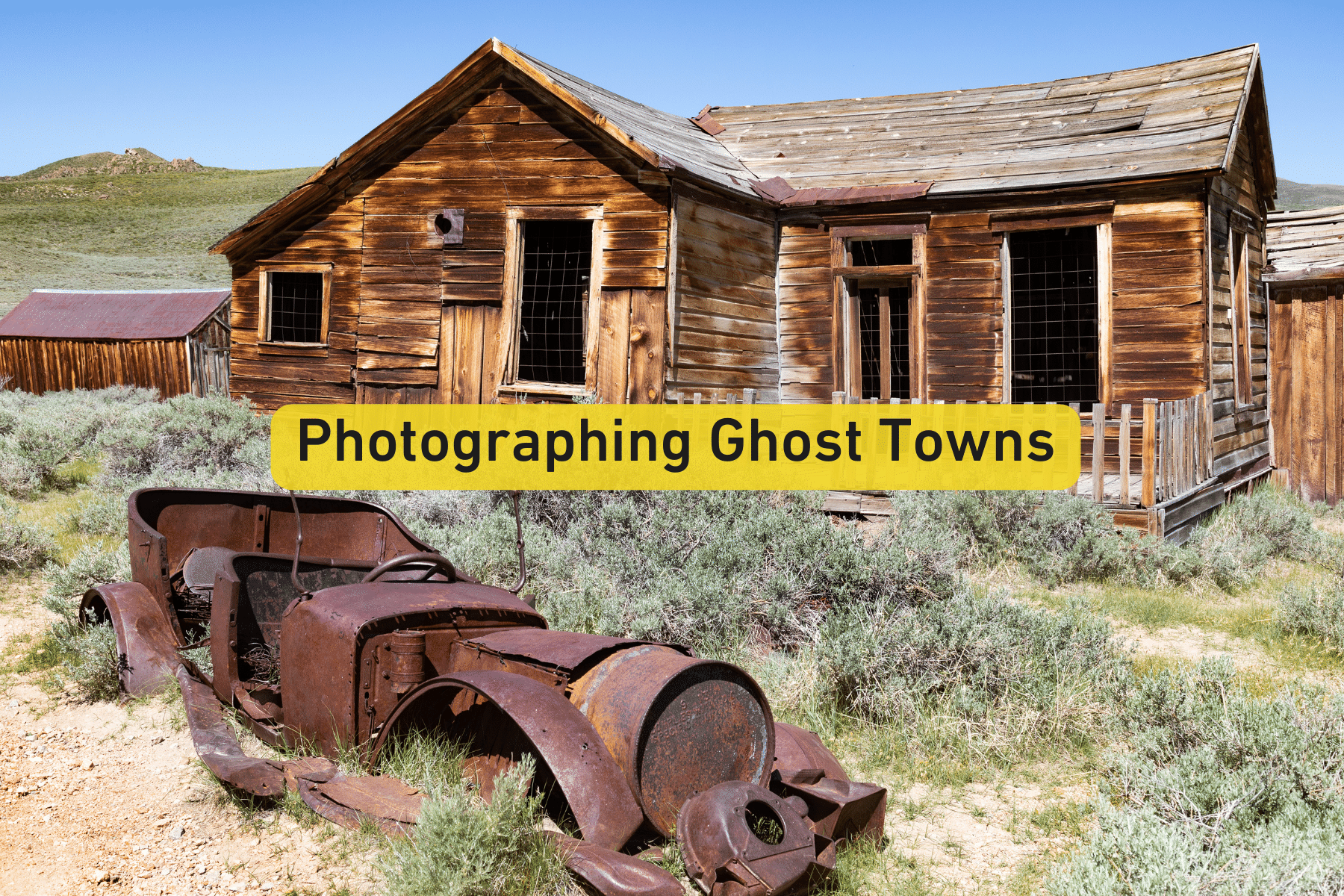 Weathered wooden ghost town building beside an old rusted car in a grassy field.