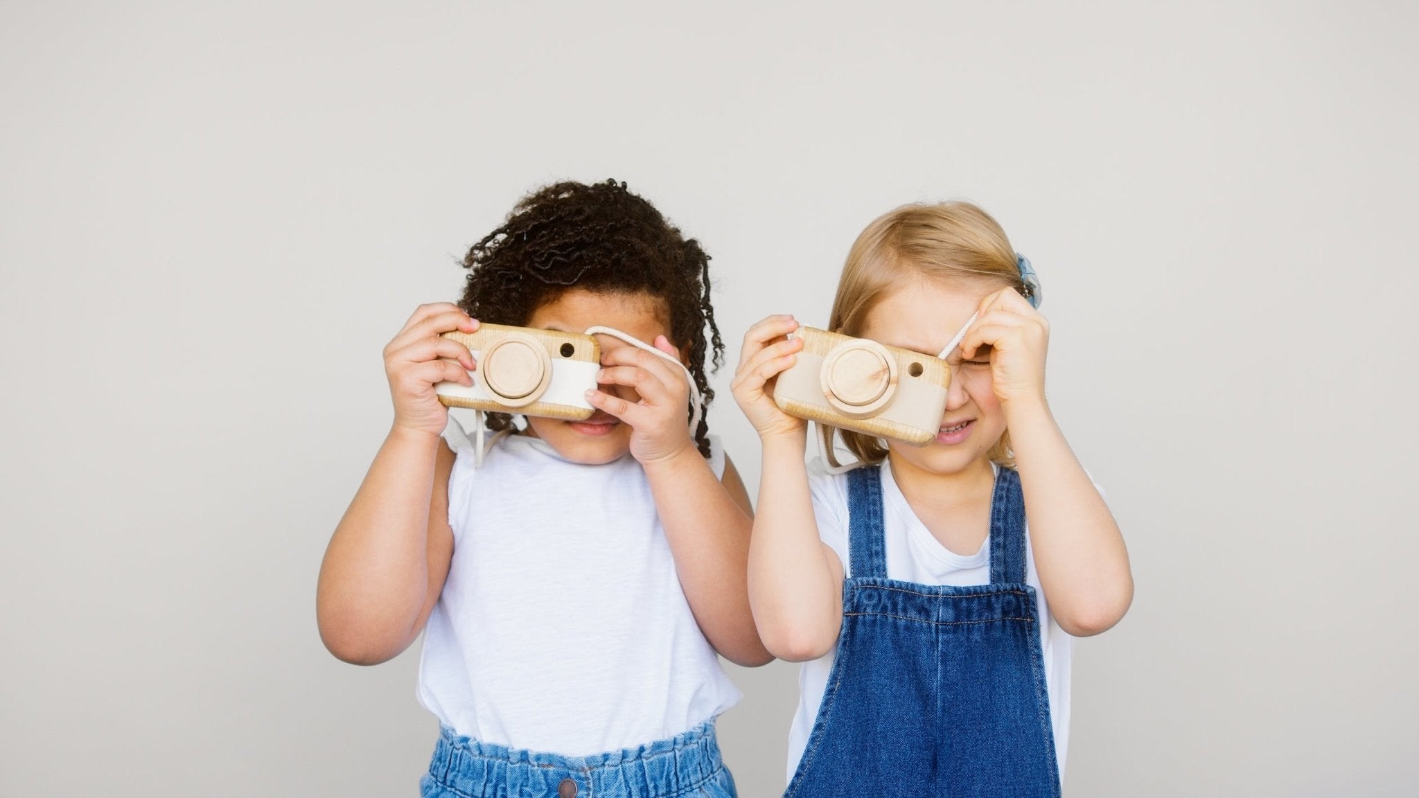 Two children holding wooden cameras, smiling and looking through the viewfinders.