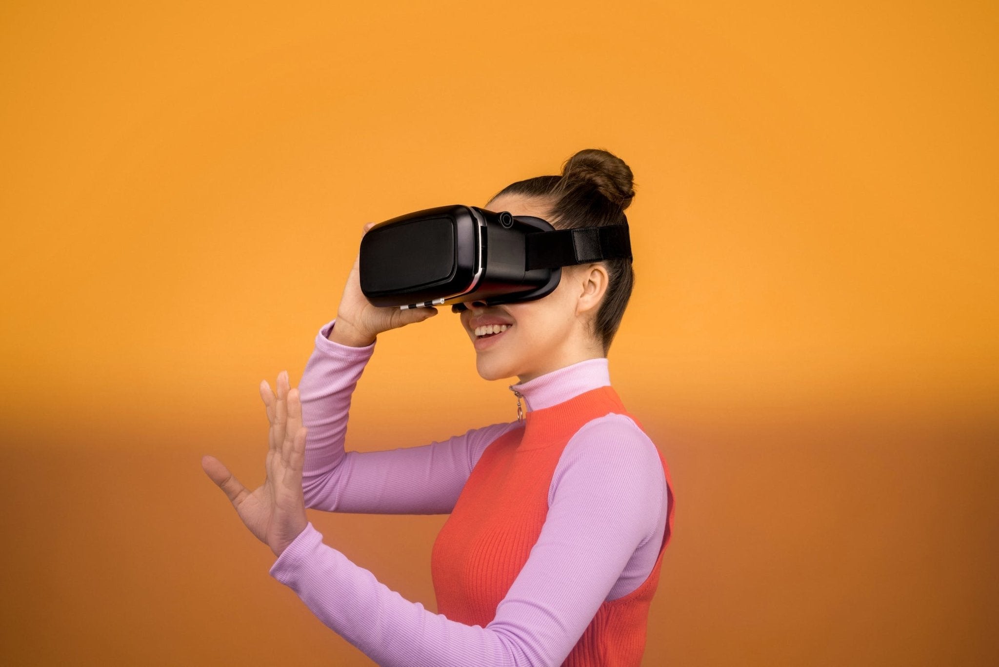 Smiling woman wearing virtual reality headset against an orange background.