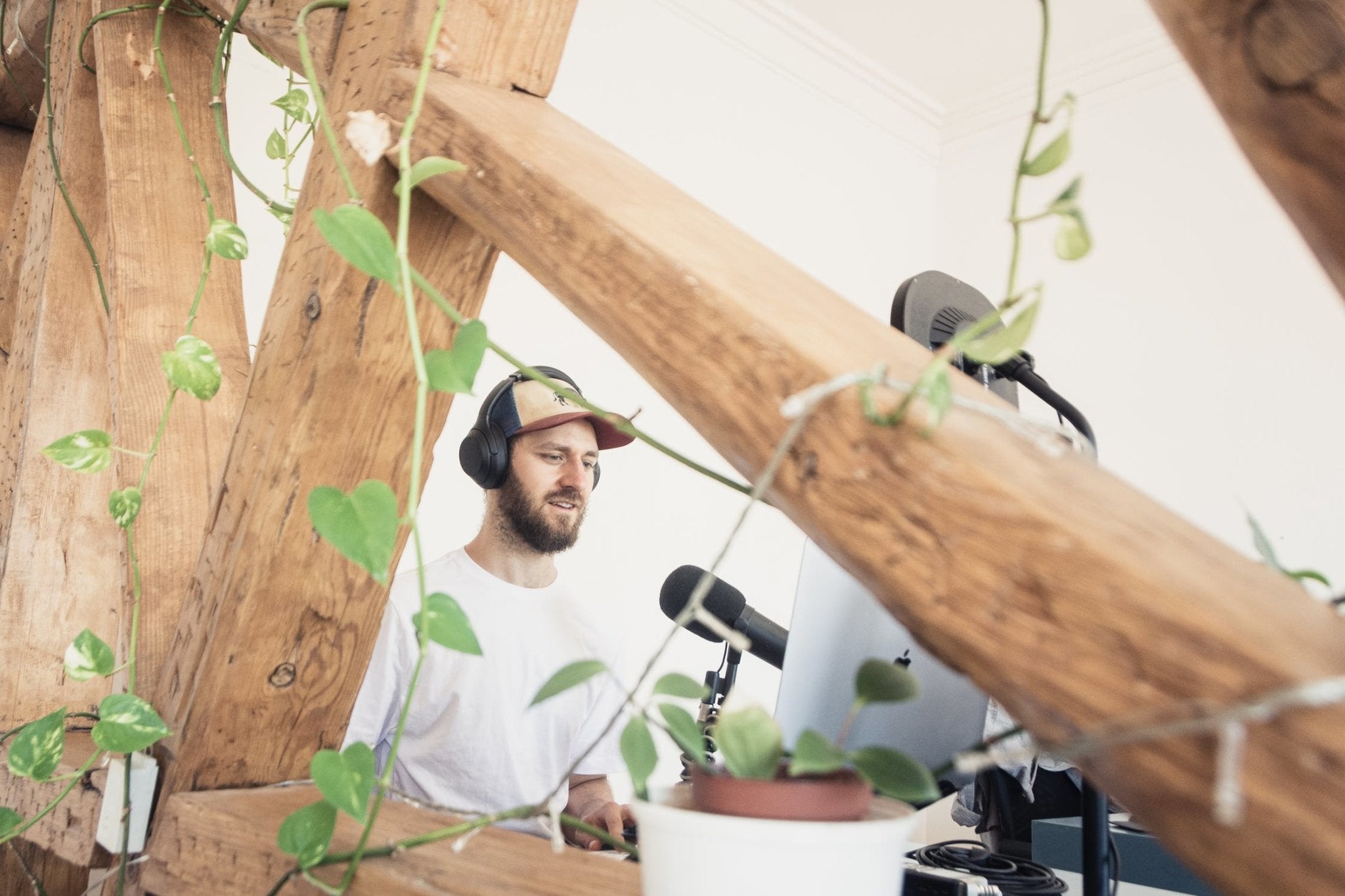 Man wearing headphones speaking into a microphone surrounded by wooden beams and plants.