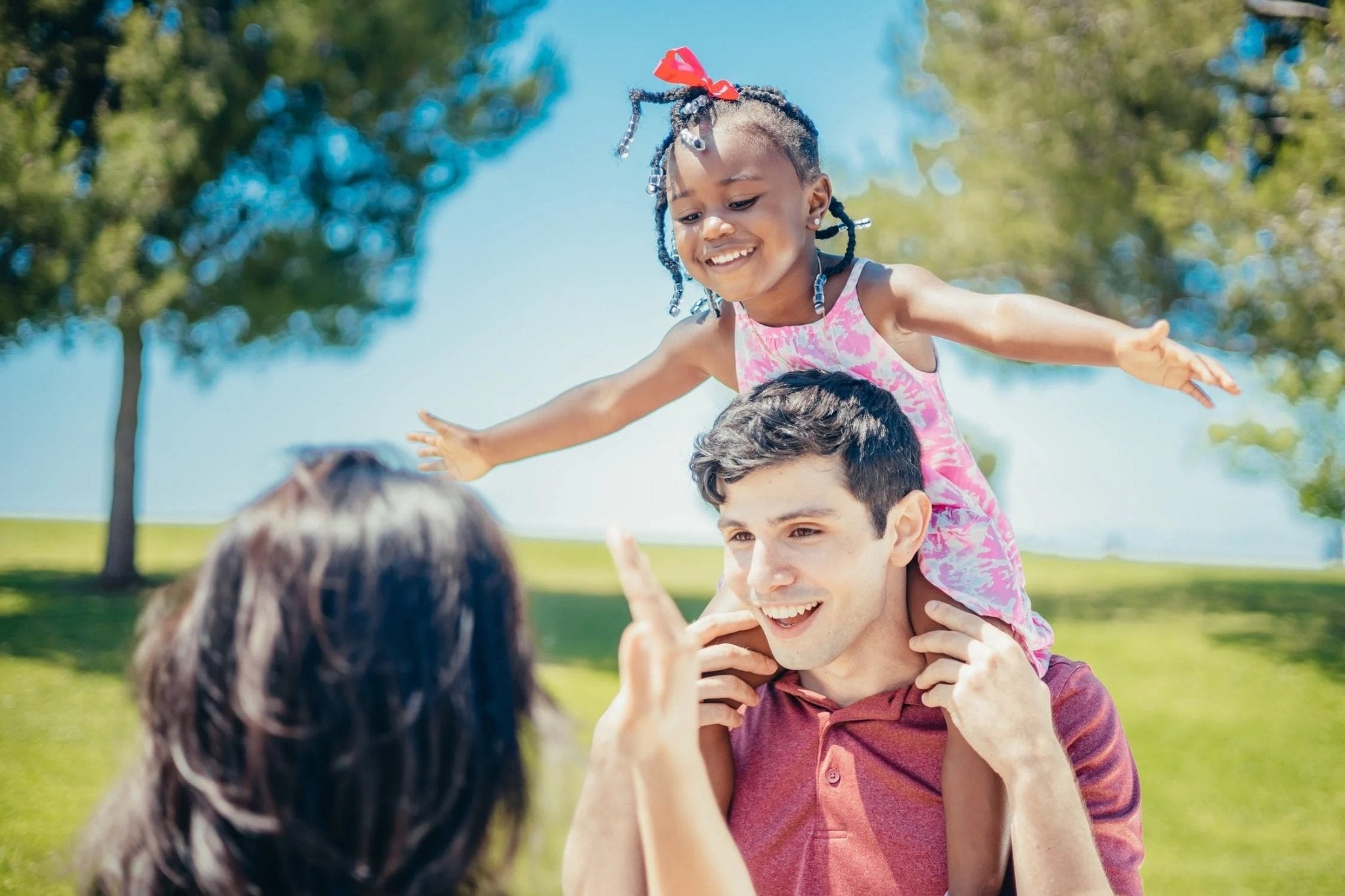 Happy family enjoying a sunny day outdoors, a father carries his daughter on his shoulders.