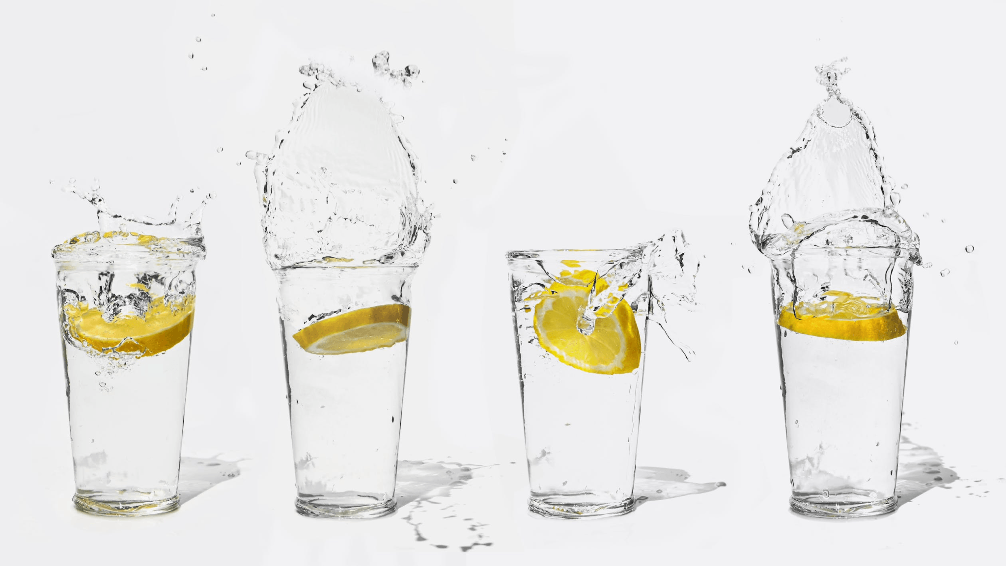 Clear glasses of water splashing with lemon slices, showing dynamic water movement.