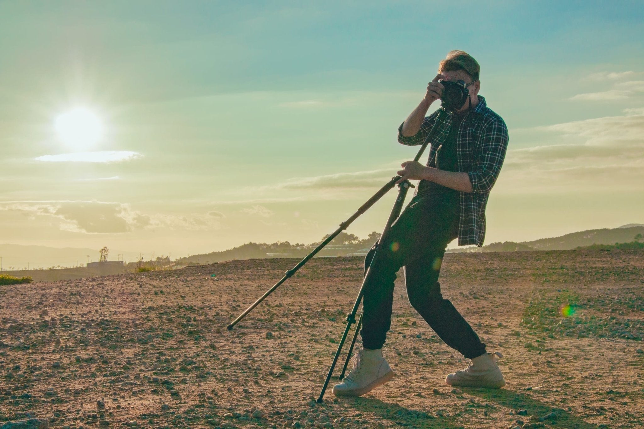 Person photographing a sunset with a camera on a tripod in a scenic outdoor setting.