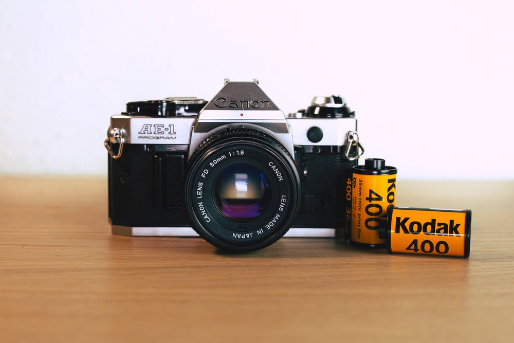 black Canon AE1 camera with lens, beside Kodak 400 film canisters.