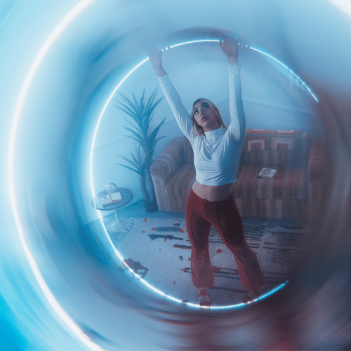 Blue halo light ring → person in a white top and red pants → striking a pose in a cozy room.