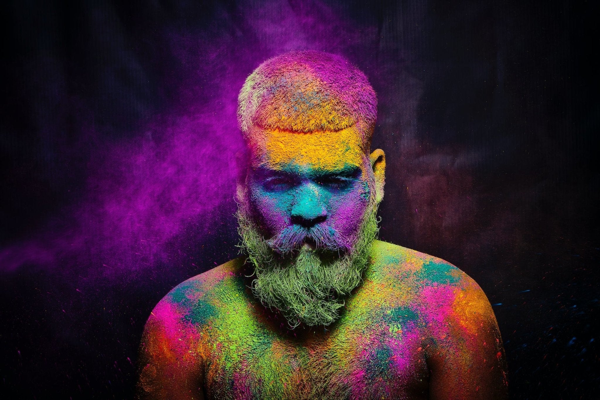Colorful powder covering a man with a beard against a dark background.