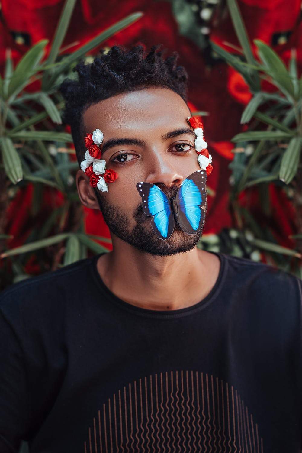 Portrait of a man with flowers and a blue butterfly on his lips, set against a floral background.